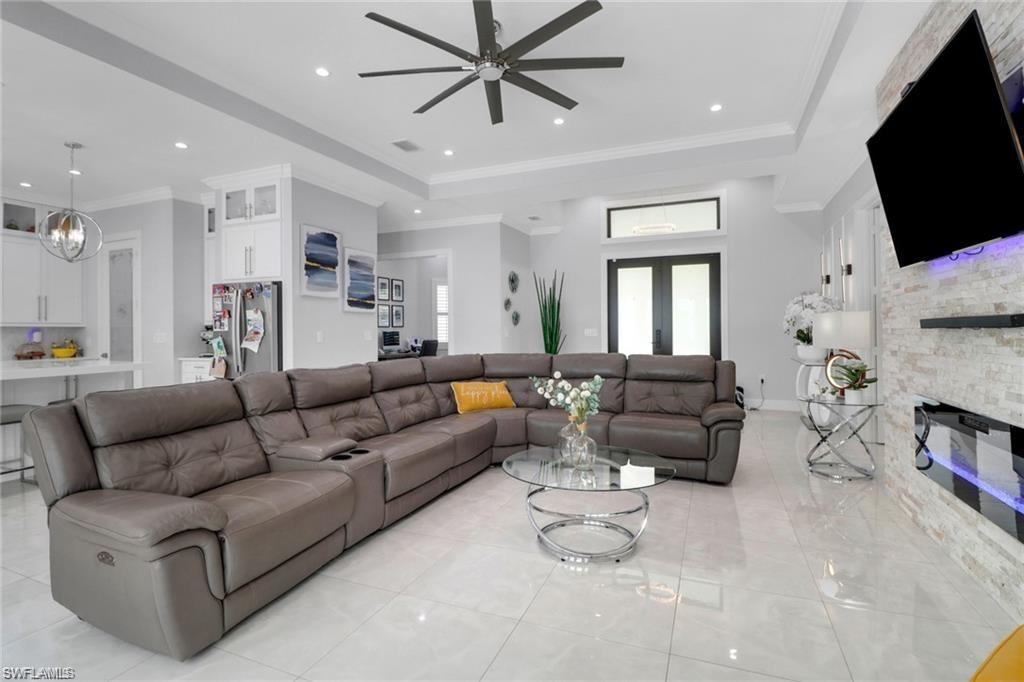 Living room featuring crown molding, a stone fireplace, a ceiling fan, a raised ceiling, and suspended lighting