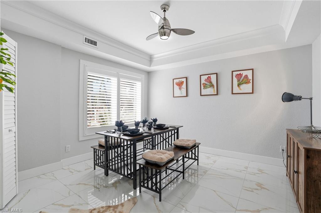 Dining area featuring ceiling fan, a raised ceiling, ornamental molding, light marble finish floors, and a desk