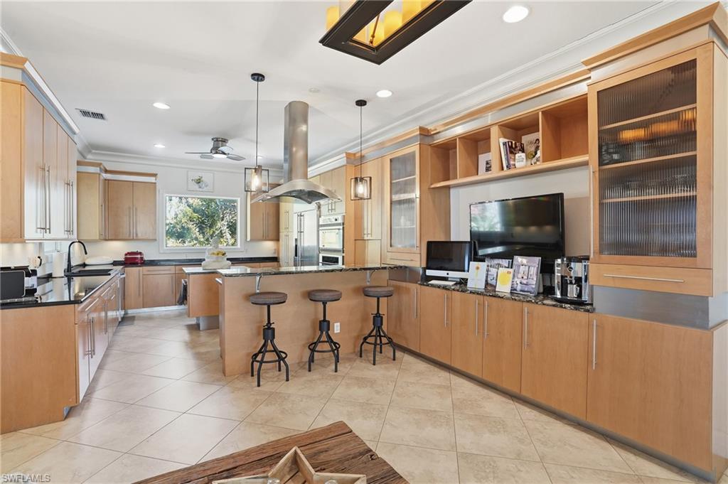Kitchen featuring a kitchen breakfast bar, dark stone countertops, crown molding, island range hood, and open shelves