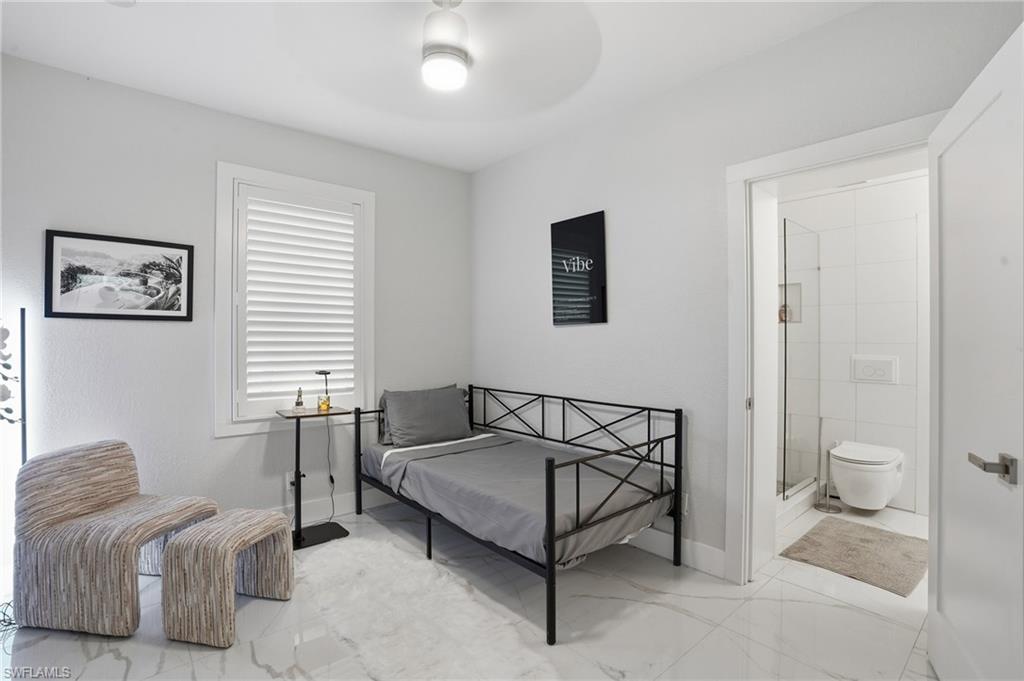 Bedroom with a ceiling fan, light marble finish floors, and ensuite bath