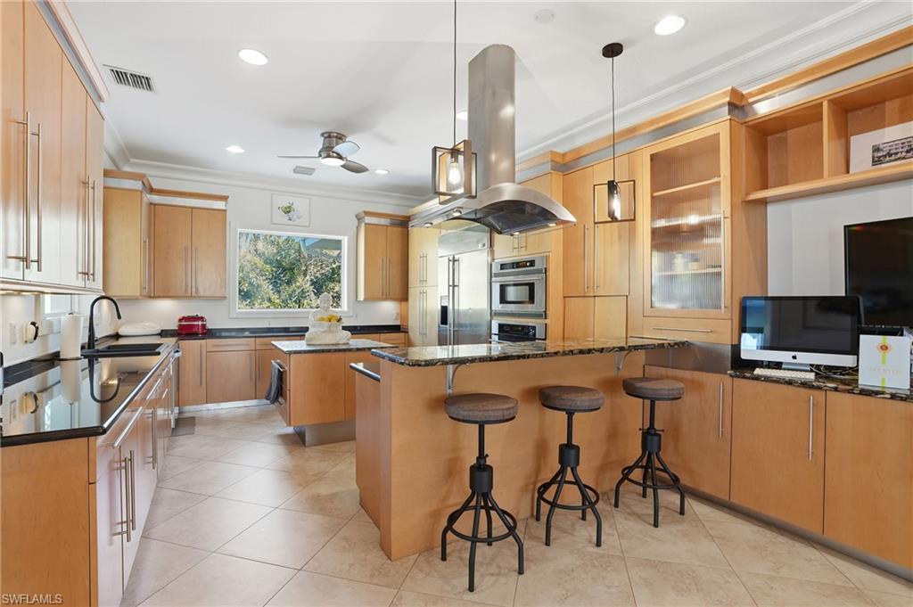 Kitchen featuring crown molding, glass fronted cabinets, a kitchen breakfast bar, island exhaust hood, and open shelves