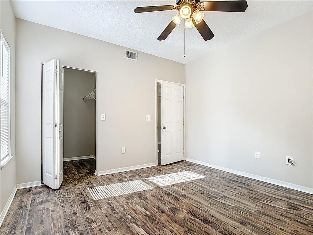 Unfurnished bedroom featuring a spacious closet, a textured ceiling, dark wood-style floors, and ceiling fan