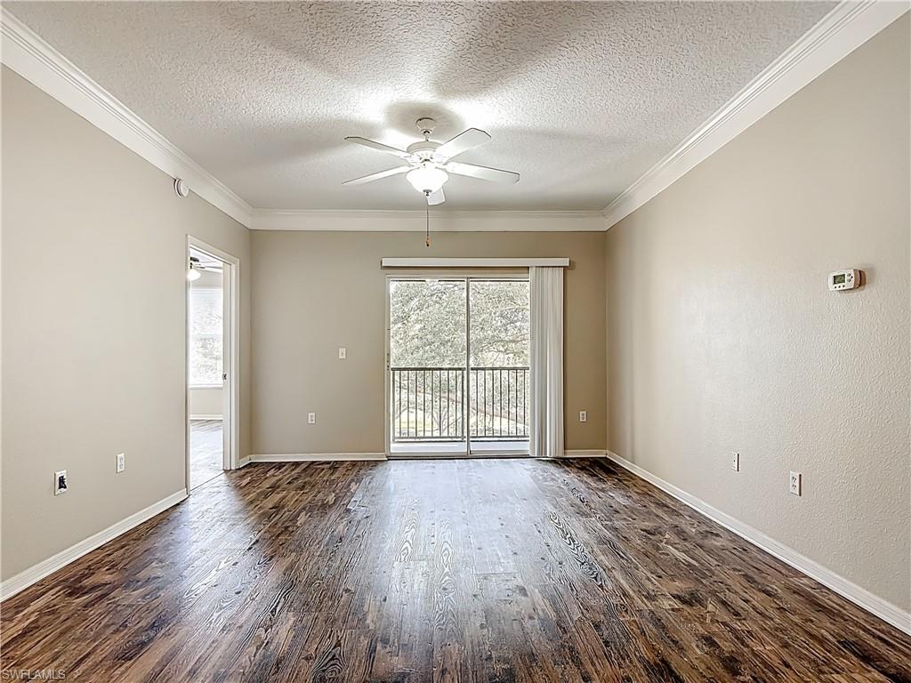 Unfurnished room featuring a textured ceiling, dark wood-type flooring, ornamental molding, and a ceiling fan