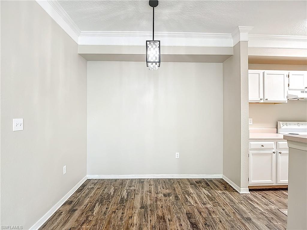 Unfurnished dining area with dark wood-style flooring, a textured ceiling, and ornamental molding