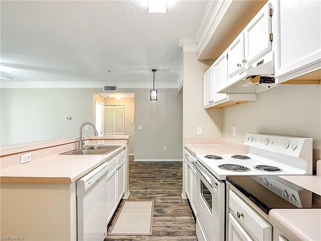 Kitchen with white appliances, white cabinets, crown molding, light countertops, and a textured ceiling