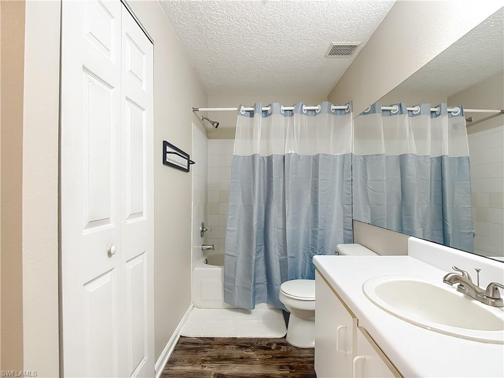 Bathroom with a textured ceiling, shower / bath combination with curtain, dark wood-style floors, vanity, and a closet