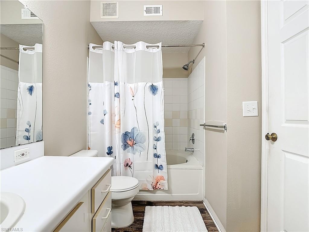 Bathroom featuring shower / tub combo with curtain, a textured ceiling, vanity, and dark wood finished floors
