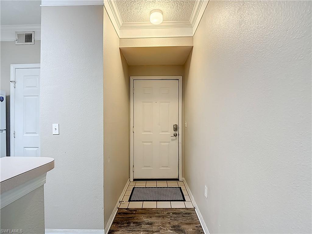 Entryway with a textured wall, wood finished floors, a textured ceiling, and crown molding