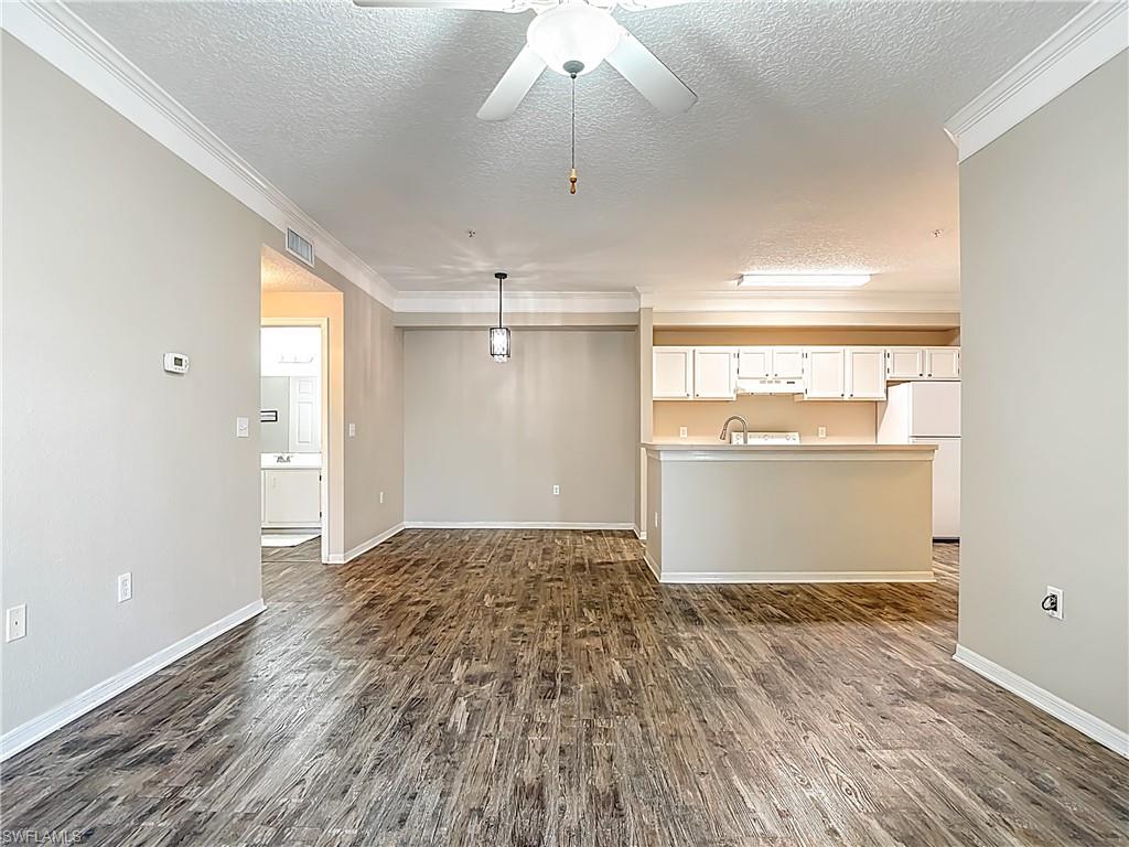 Unfurnished living room featuring ceiling fan, ornamental molding, dark wood-type flooring, and a textured ceiling