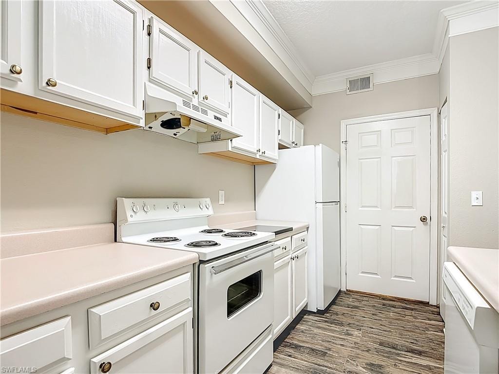 Kitchen featuring white appliances, white cabinetry, light countertops, crown molding, and dark wood finished floors