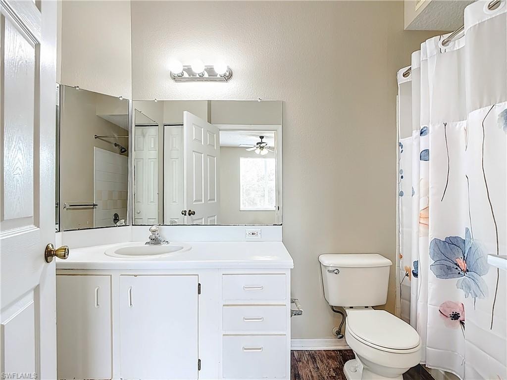 Full bath with vanity, dark wood-type flooring, a textured wall, and a ceiling fan