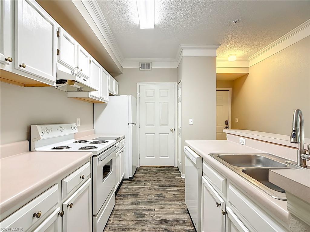 Kitchen with white cabinets, white appliances, a textured ceiling, light countertops, and dark wood-style floors