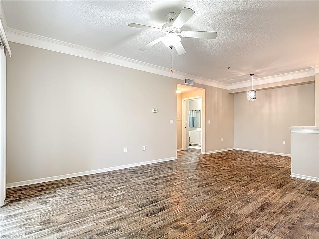 Empty room with a textured ceiling, a ceiling fan, dark wood finished floors, and ornamental molding