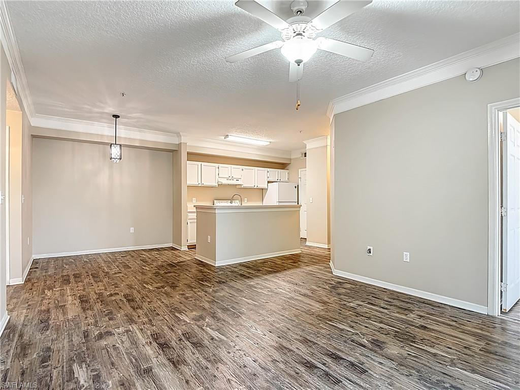 Unfurnished living room with a textured ceiling, dark wood-style floors, ornamental molding, and a ceiling fan