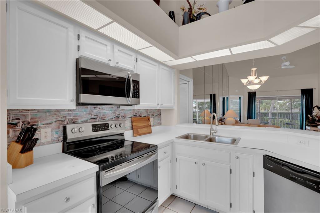 Kitchen with appliances with stainless steel finishes, white cabinets, light tile patterned floors, and decorative backsplash