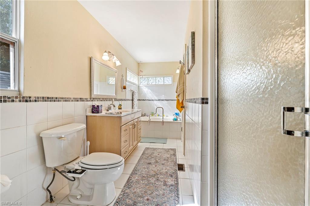 Full bath with a garden tub, tile walls, vanity, light tile patterned floors, and a shower stall