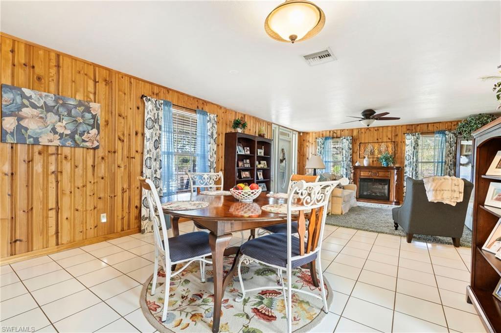 Dining space featuring a glass covered fireplace, light tile patterned floors, wood walls, and a ceiling fan