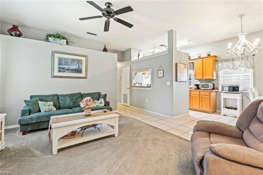Living area with light tile patterned floors, a chandelier, ceiling fan, and light colored carpet