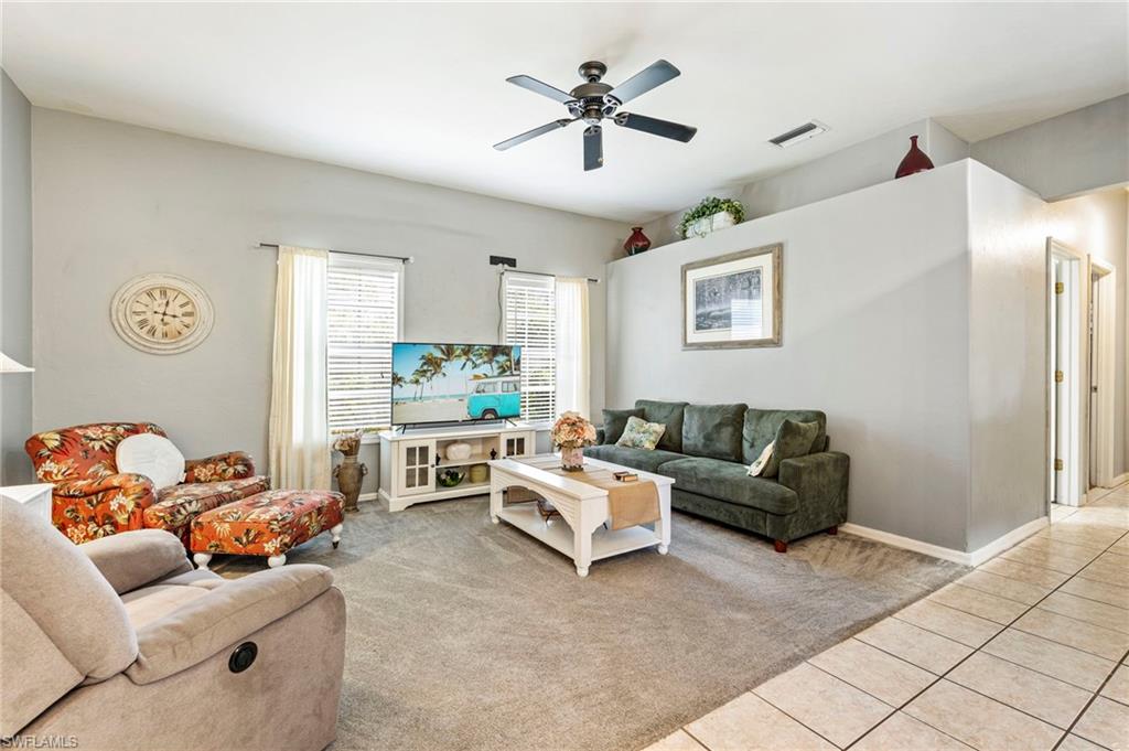 Carpeted living room with a ceiling fan and tile patterned floors