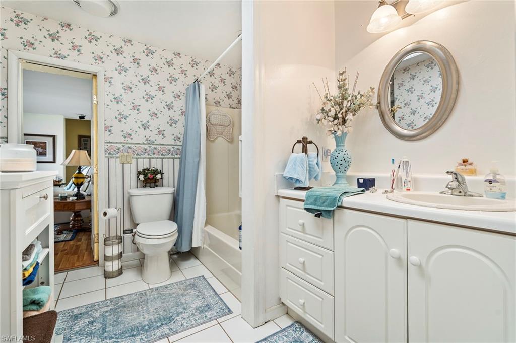 Bathroom with vanity, shower / tub combo, wainscoting, light tile patterned floors, and wallpapered walls