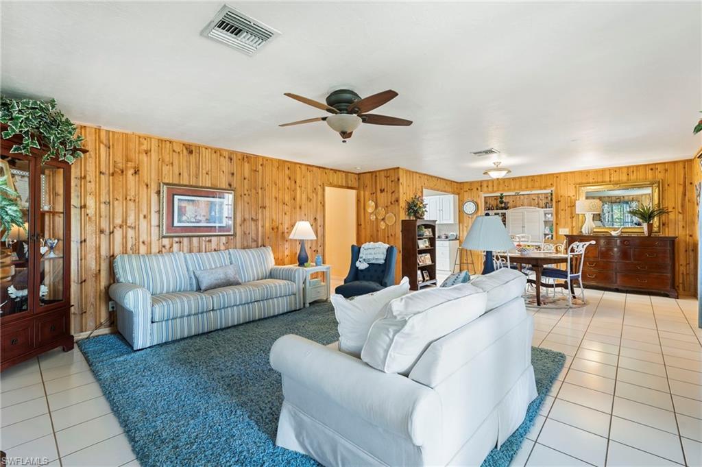 Living room featuring light tile patterned floors, a ceiling fan, and wooden walls