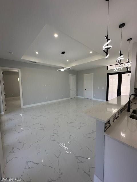 Kitchen featuring pendant lighting, a tray ceiling, light stone counters, light marble finish floors, and open floor plan