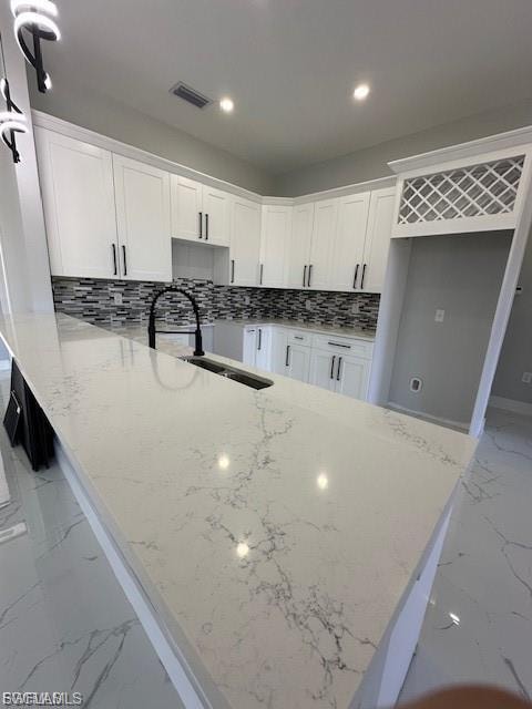 Kitchen with a peninsula, light stone countertops, white cabinetry, tasteful backsplash, and recessed lighting
