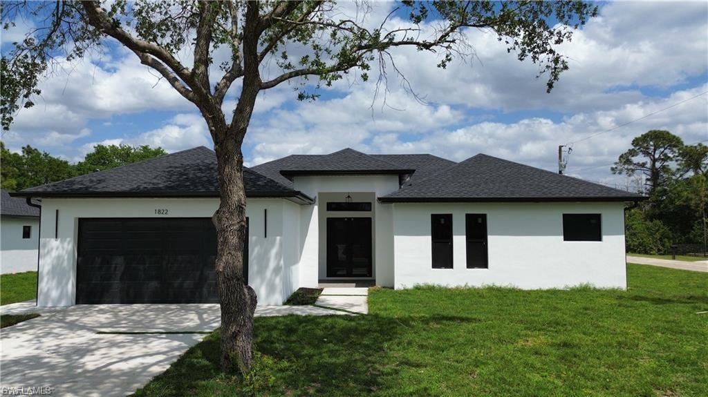 Prairie-style home with a front lawn, driveway, a shingled roof, and stucco siding