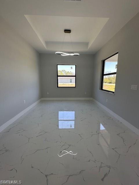 Empty room with a raised ceiling, plenty of natural light, and light marble finish flooring