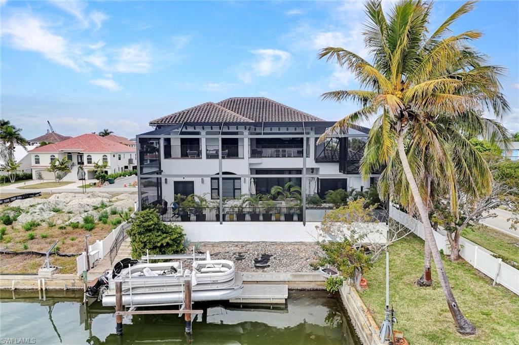 Rear view of house featuring a water view, a tiled roof, boat lift, and stucco siding