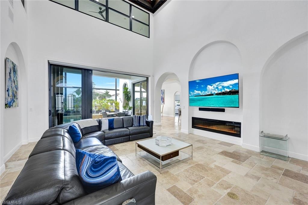 Living area with stone tile flooring, a glass covered fireplace, arched walkways, and a high ceiling