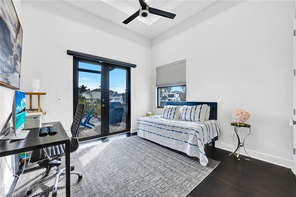 Bedroom featuring an office area, a high ceiling, french doors, dark wood-style floors, and a ceiling fan