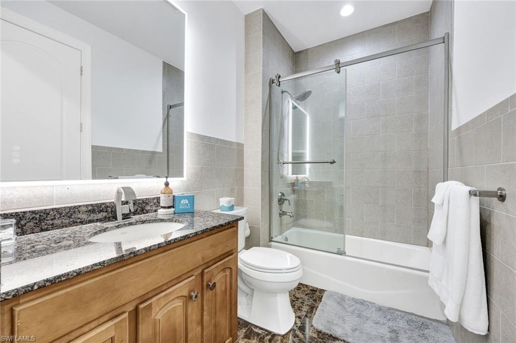 Full bathroom with tile walls, shower / bath combination with glass door, vanity, and wainscoting