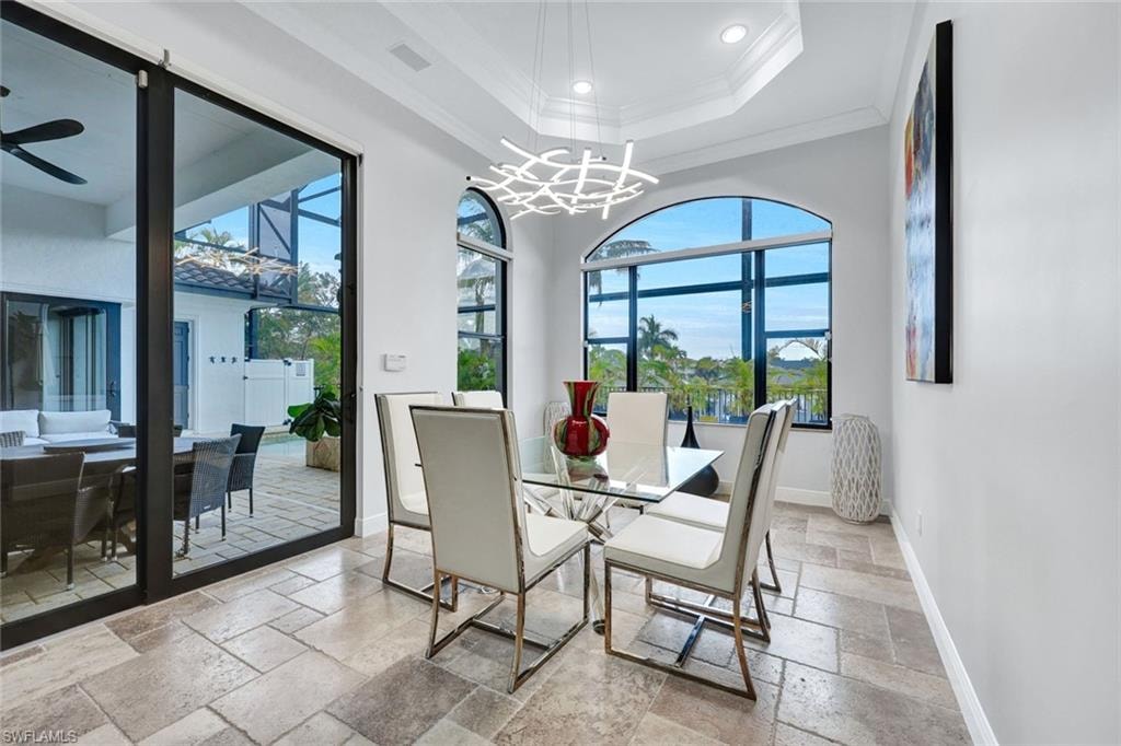 Dining space with stone tile flooring, a ceiling fan, healthy amount of natural light, crown molding, and hanging lights
