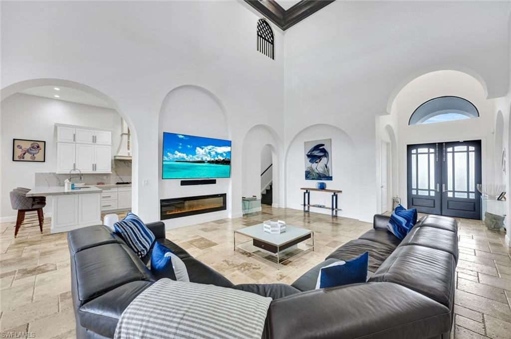 Living area with stone tile flooring, arched walkways, a high ceiling, french doors, and a glass covered fireplace