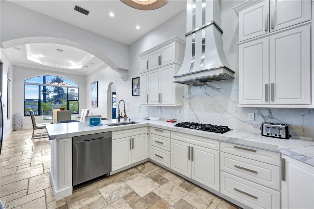 Kitchen with a raised ceiling, light stone counters, white cabinets, dishwasher, and a peninsula