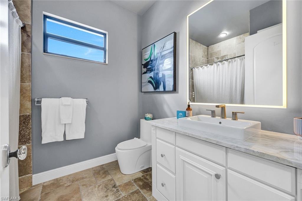Bathroom featuring vanity, curtained shower, and light stone finish floors