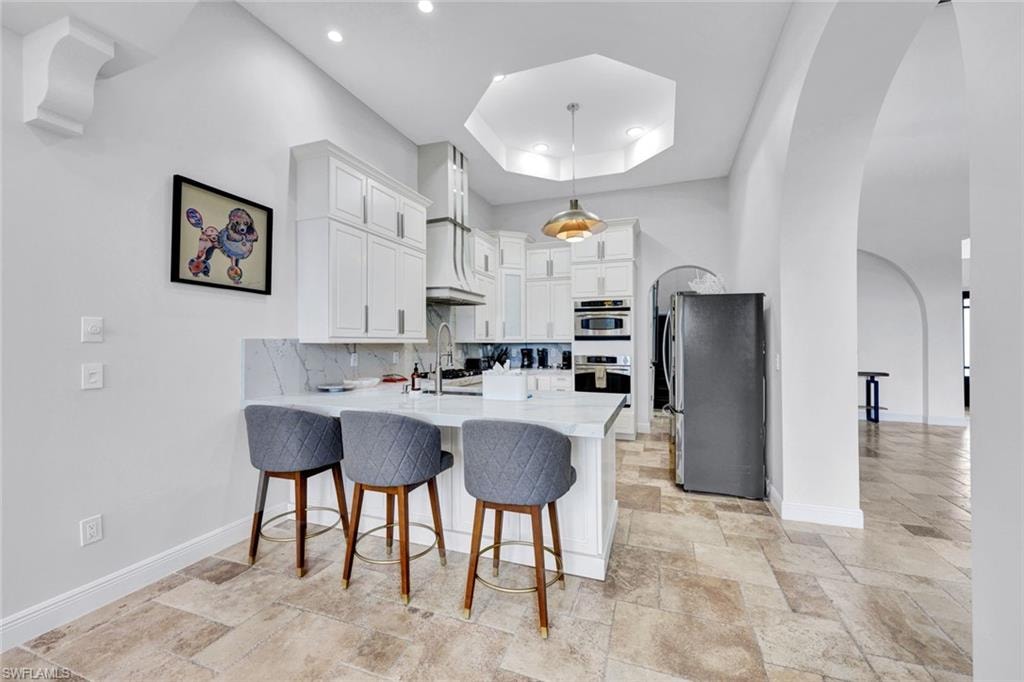 Kitchen featuring arched walkways, a breakfast bar, decorative backsplash, a peninsula, and white cabinets