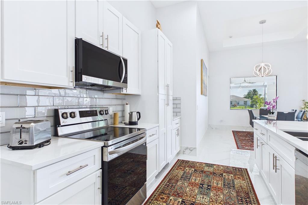 Kitchen featuring stainless steel appliances, white cabinets, decorative light fixtures, light stone counters, and a tray ceiling