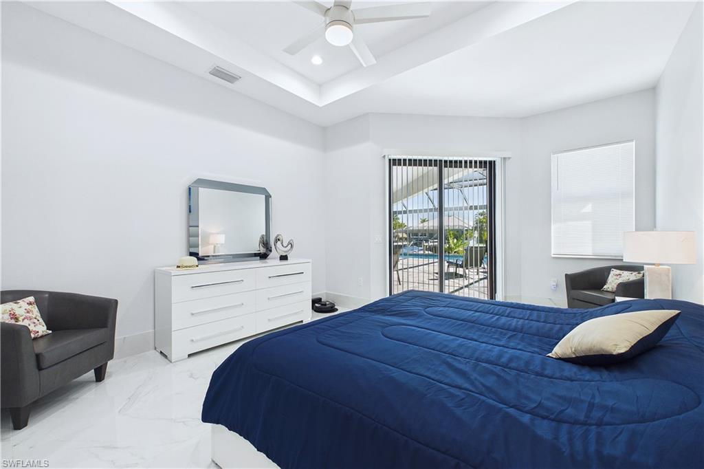Bedroom featuring access to exterior, a raised ceiling, a ceiling fan, recessed lighting, and light marble finish flooring