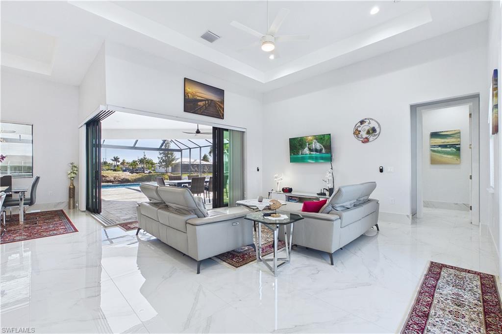 Living room featuring a sunroom, ceiling fan, a raised ceiling, and light marble finish floors