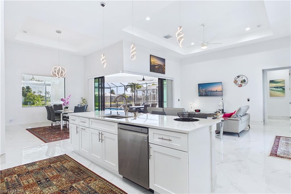 Kitchen featuring open floor plan, white cabinets, decorative light fixtures, stainless steel dishwasher, and light stone counters