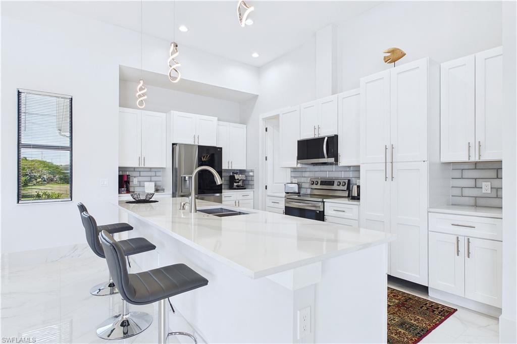 Kitchen featuring stainless steel appliances, backsplash, a breakfast bar, white cabinets, and light stone counters