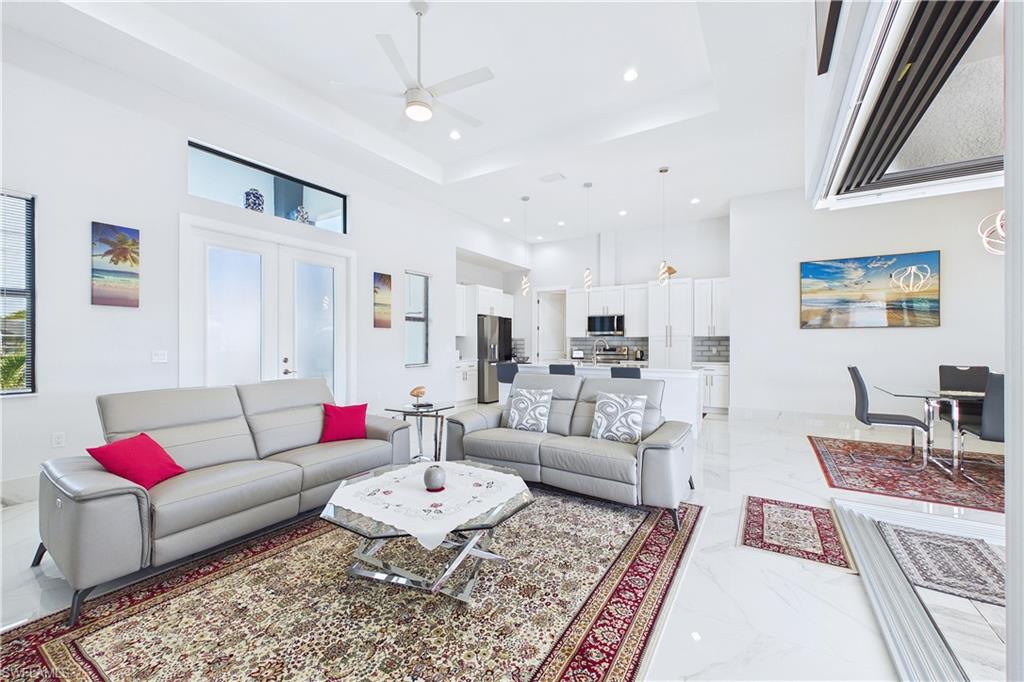 Living area featuring light marble finish flooring, recessed lighting, a high tray ceiling, ceiling fan, and french doors