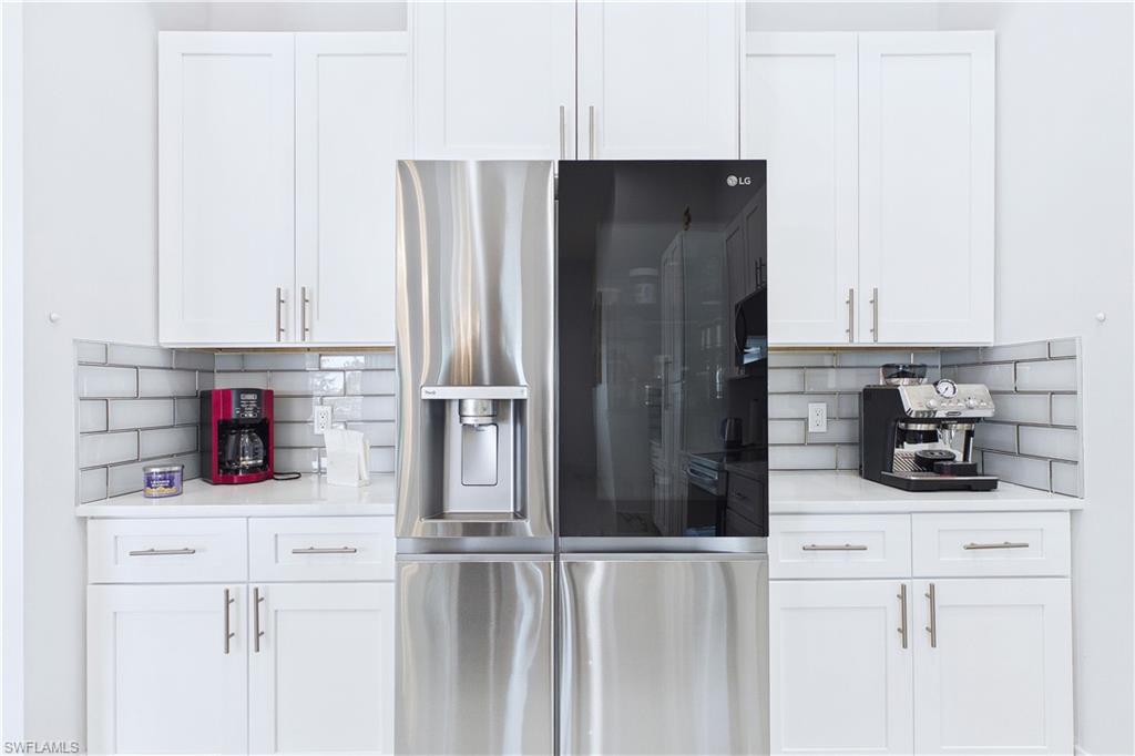 Kitchen featuring stainless steel fridge, white cabinets, backsplash, and light stone countertops