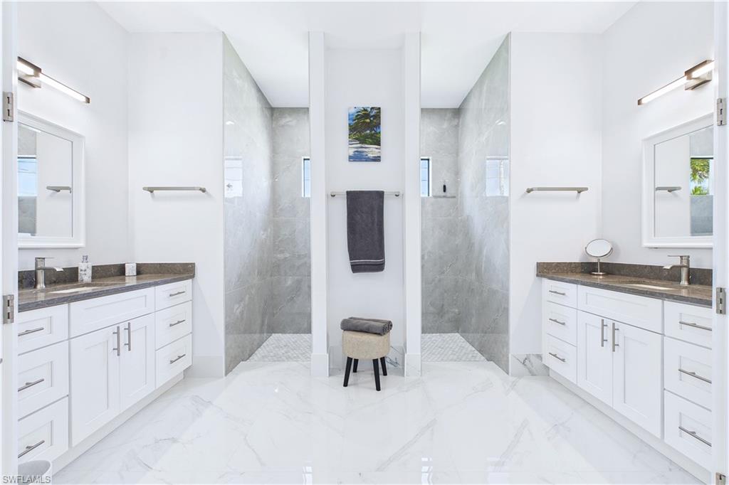 Full bathroom featuring a marble finish shower, two vanities, and healthy amount of natural light