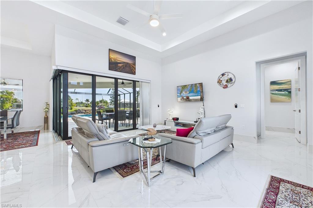 Living room with light marble finish floors, a high tray ceiling, and ceiling fan