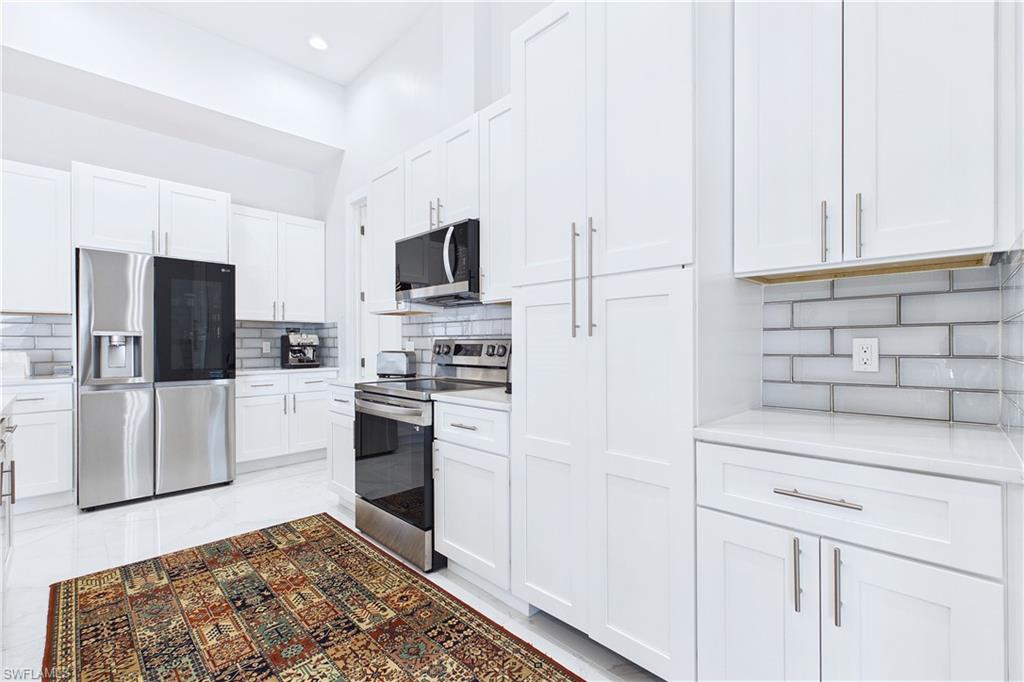 Kitchen featuring stainless steel appliances, white cabinets, decorative backsplash, light stone counters, and recessed lighting