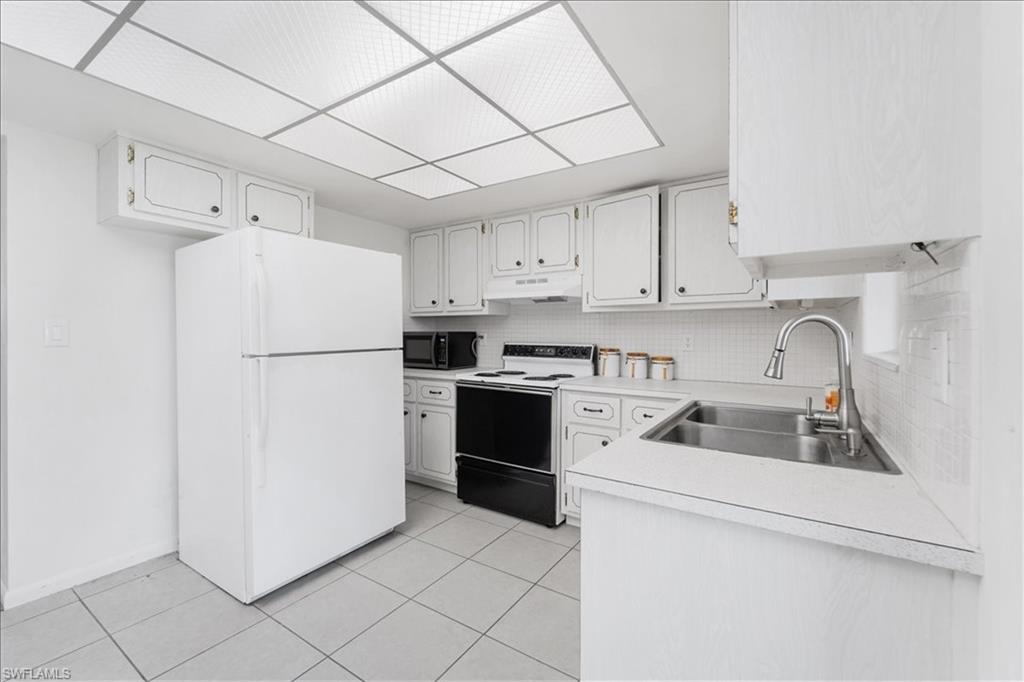 Kitchen with freestanding refrigerator, light countertops, range with electric cooktop, and white cabinetry
