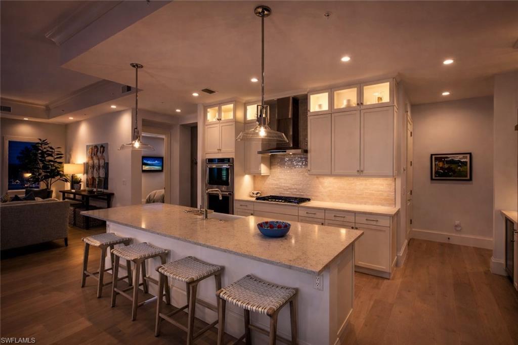 Kitchen with a kitchen breakfast bar, open floor plan, glass insert cabinets, dark wood finished floors, and decorative light fixtures